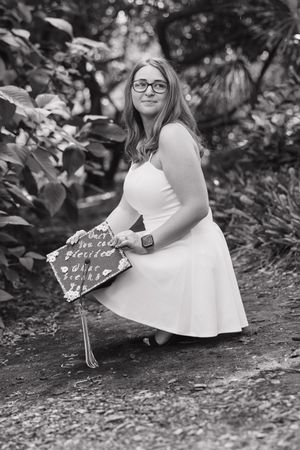 Black and white photo of someone in a white dress sitting on the ground with a small sign.