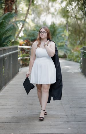 Someone in a white dress and black graduation gown walks along an outdoor pathway.