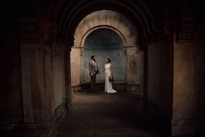 A romantic couple poses in a dimly lit stone archway at a historic venue.