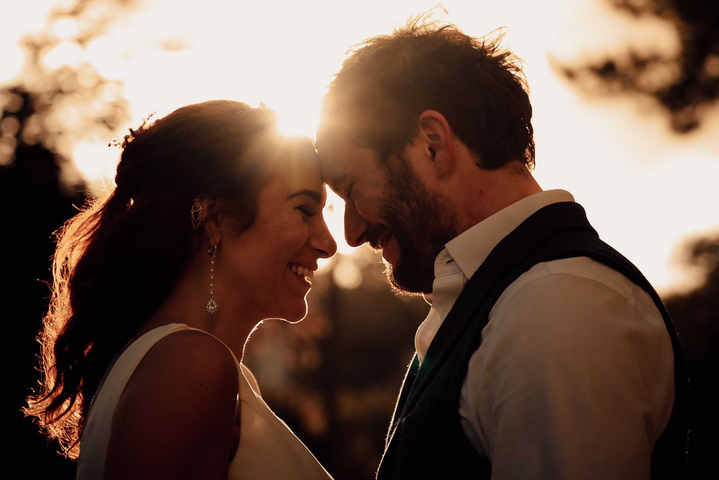 Sunset wedding portrait with warm golden light filtering through trees.