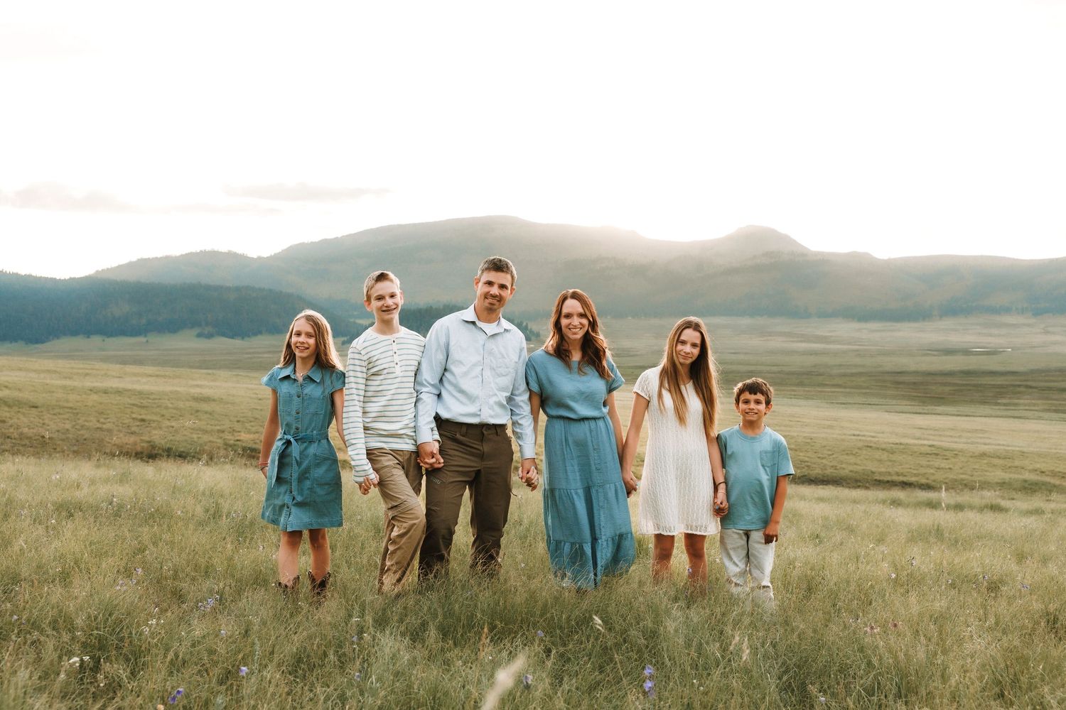 Albuquerque Family of six in coordinating blue outfits stands in open mountain meadow at sunset in the Valle Grande, Valles Caldera.