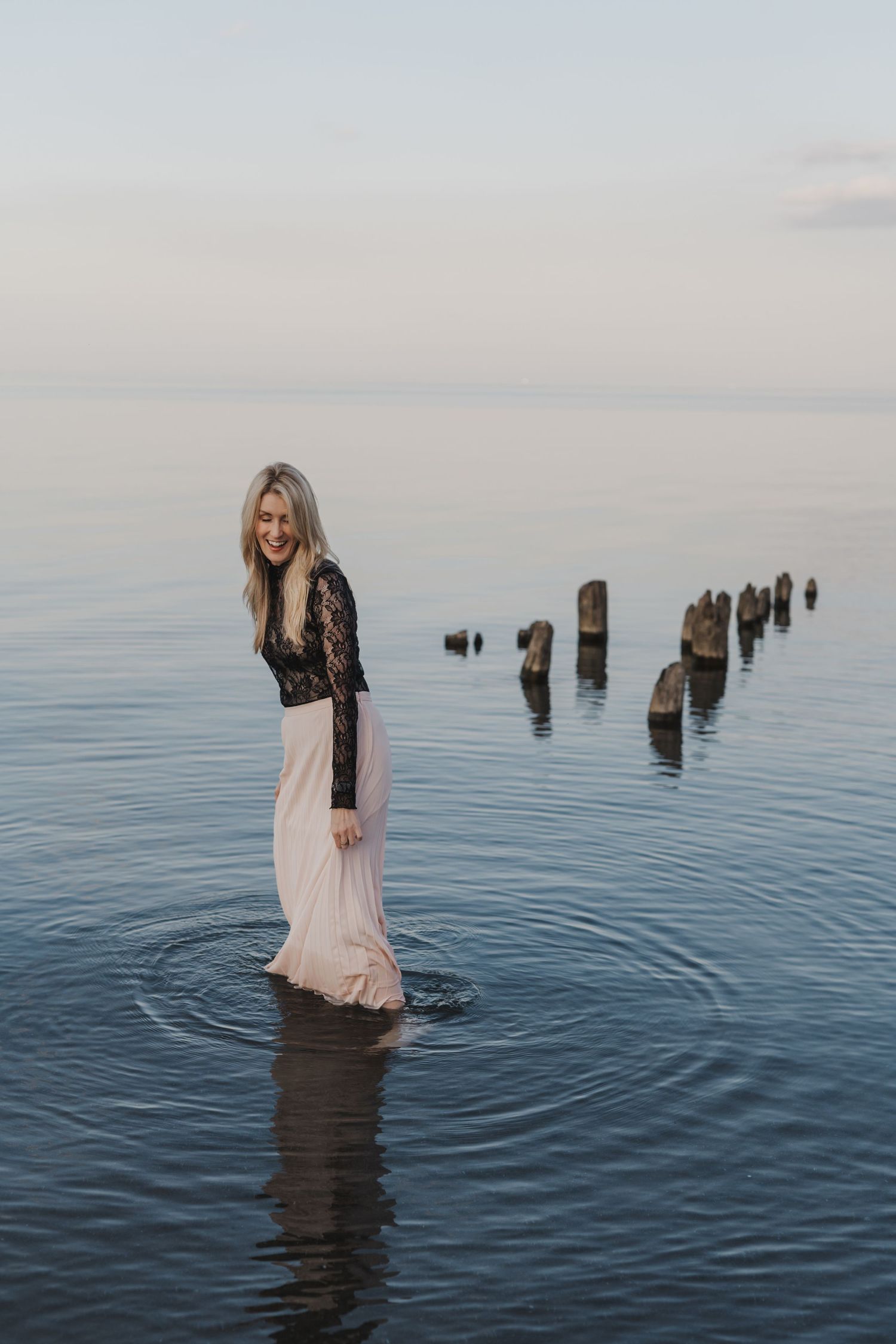 Michelle Hugill standing in calm lake water, during golden hour, holding her skirt.