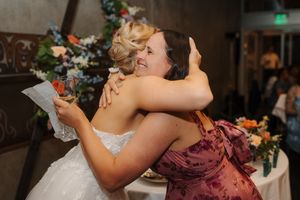 Two people share an emotional embrace during a wedding celebration with floral decorations in the background.