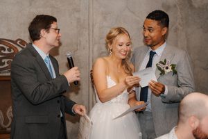 Wedding party members laugh and share drinks during a reception celebration in a rustic venue.