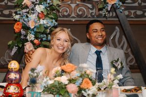 A wedding celebration with floral arrangements featuring peach and coral roses alongside blue accents in an elegant venue.