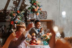 Colorful floral centerpiece with orange and pink flowers adorns a rustic wooden dining table during a wedding reception.