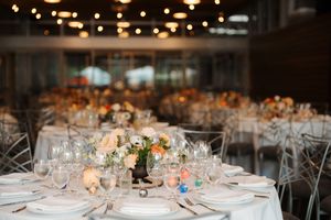 Elegant wedding reception tables set with crystal glassware, white linens, and soft floral centerpieces in a dimly lit venue.