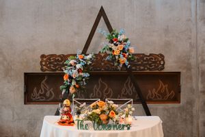 Wedding reception table decorated with floral arrangements and wooden cross decor on concrete wall.