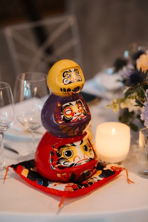 Japanese Daruma dolls displayed on a white tablecloth with candles and decorative elements at an elegant table setting.
