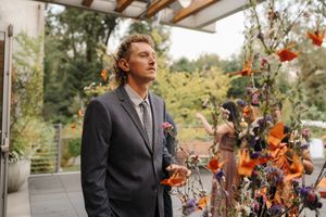 Wedding ceremony decor features vibrant orange and purple floral arrangements against a natural outdoor backdrop.