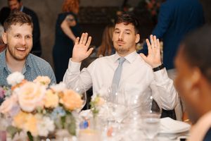 Wedding guests having fun at a reception table with floral centerpieces and animated expressions.