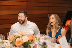 Wedding guests share a joyful moment of laughter at an elegant reception dinner with floral centerpieces.