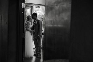 A couple stands in silhouette in a doorway on their wedding day, captured in black and white photography.
