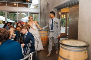Wedding celebration in a rustic winery venue with wine barrels and guests in formal attire.