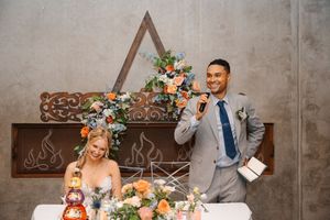 Rustic wedding ceremony setup with wooden triangle arch decorated with colorful wildflowers and greenery against concrete wall.