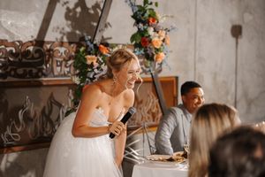 People gathered around a rustic wooden table enjoying a meal in an industrial-style dining space with floral decor.