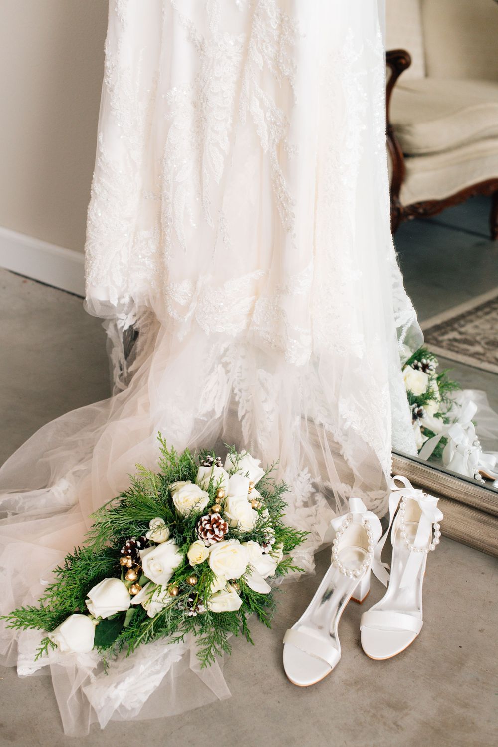 Wedding dress hem with white floral bouquet and bridal shoes on concrete floor.