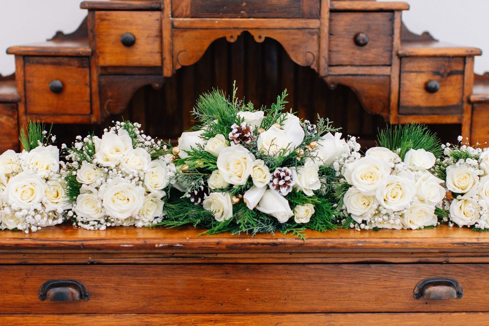 White rose and greenery wedding bouquets arranged on antique wooden dresser.