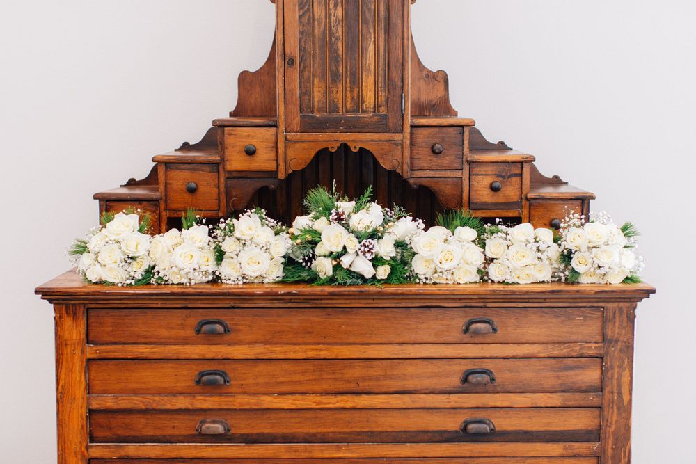 Antique wooden dresser decorated with white floral arrangements.