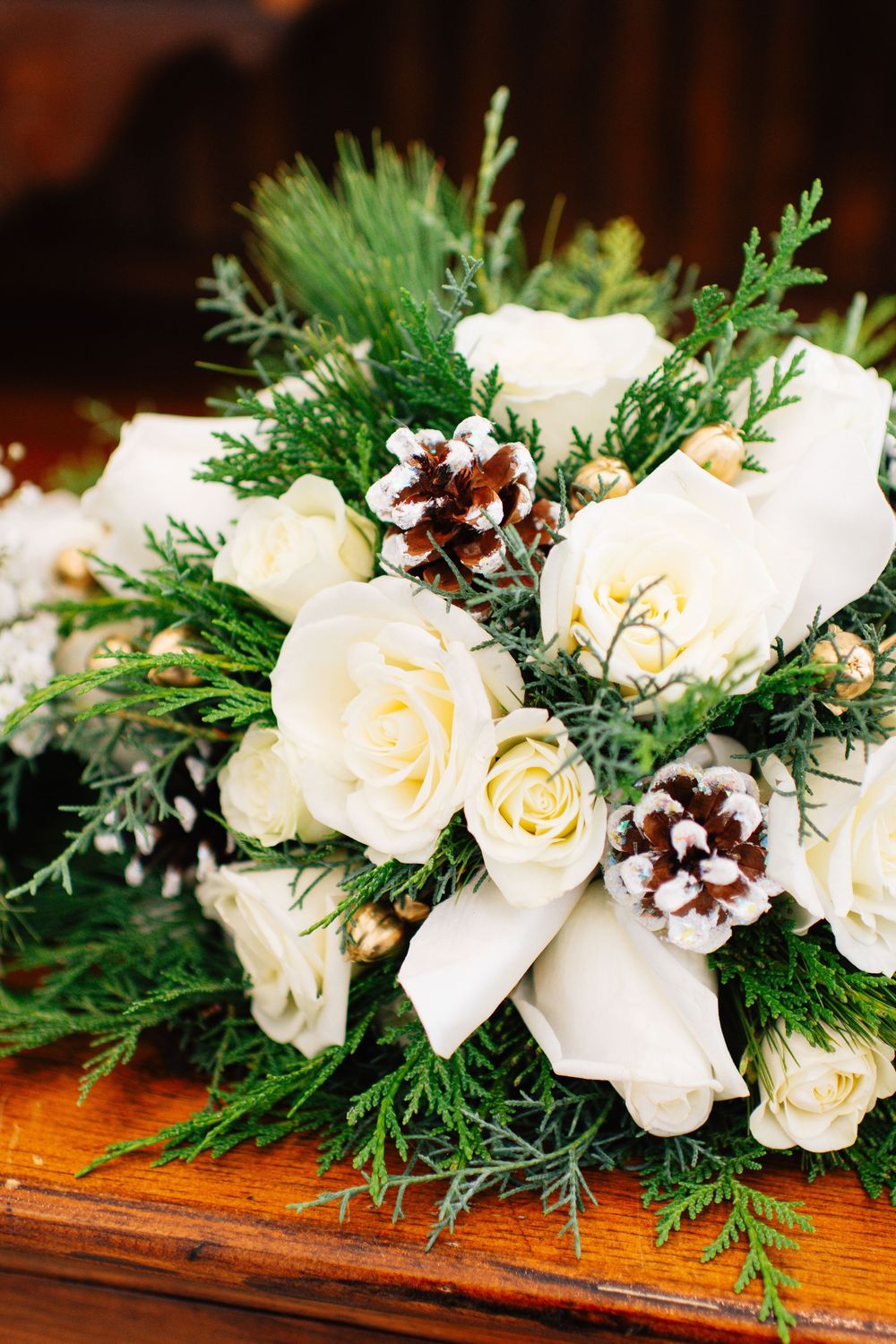 Winter wedding bouquet with white roses, pine cones, and evergreen sprigs.