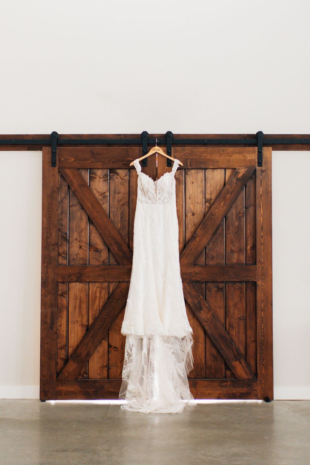 White lace wedding dress hanging on rustic wooden barn doors.