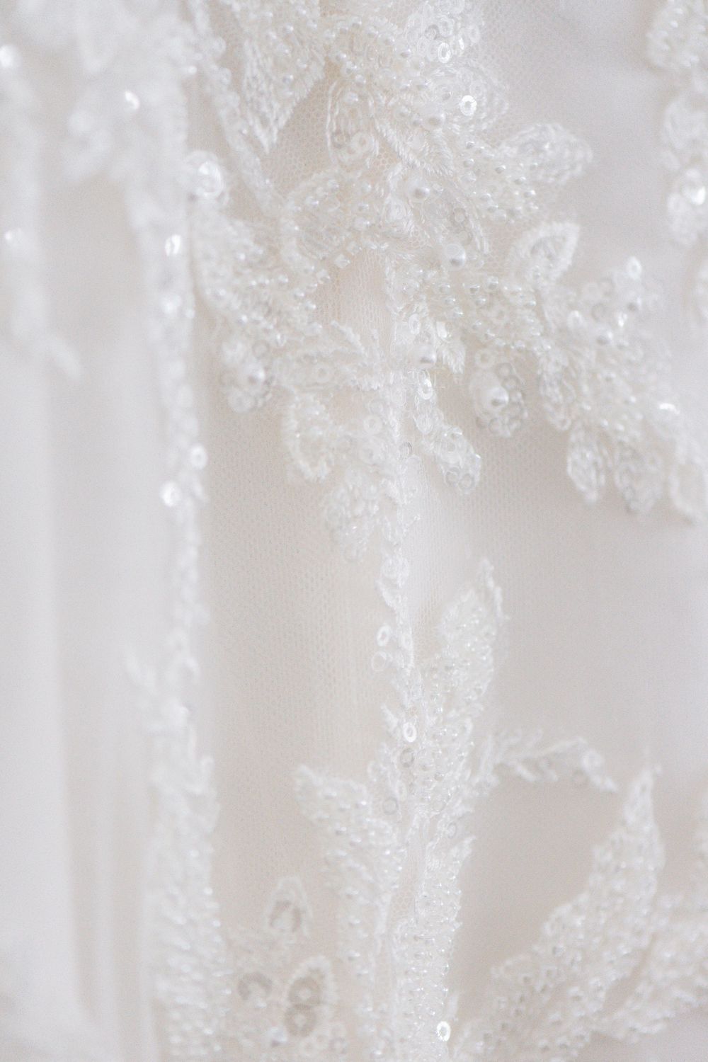 Delicate white lace and beading detail on wedding dress fabric.