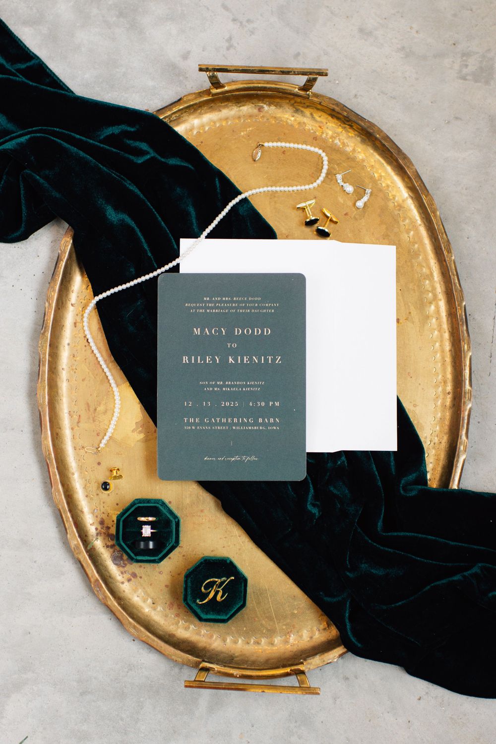 Wedding invitation suite with dark green cards and gold accents on metallic tray.