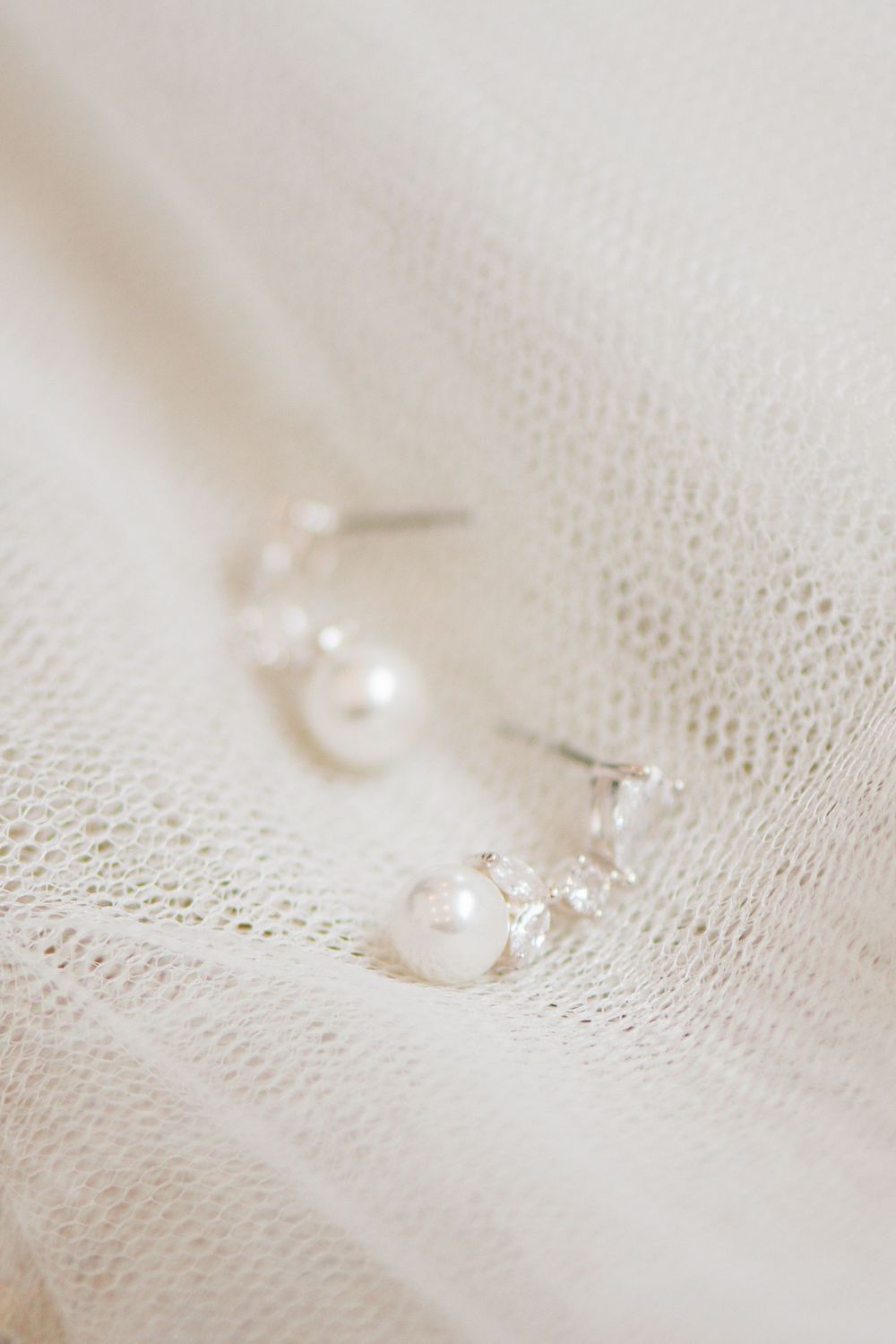 Pearl and crystal bridal earrings resting on white lace fabric.