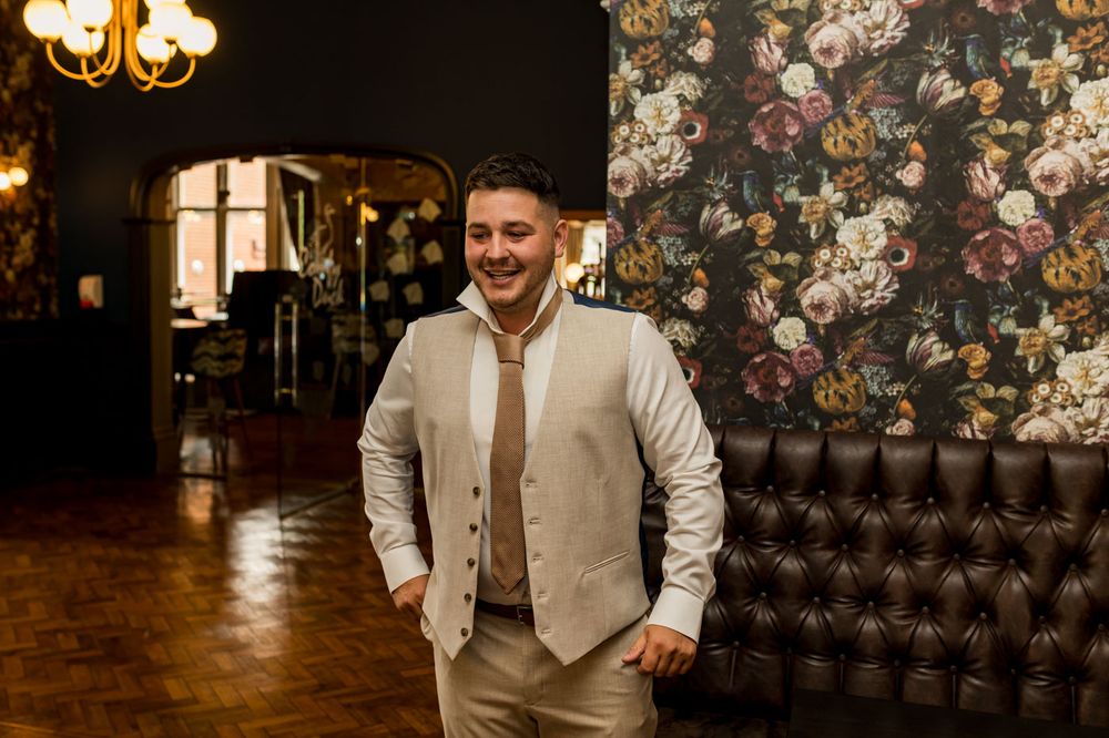 Candid moments of groomsmen enjoying themselves against vintage floral wallpaper.