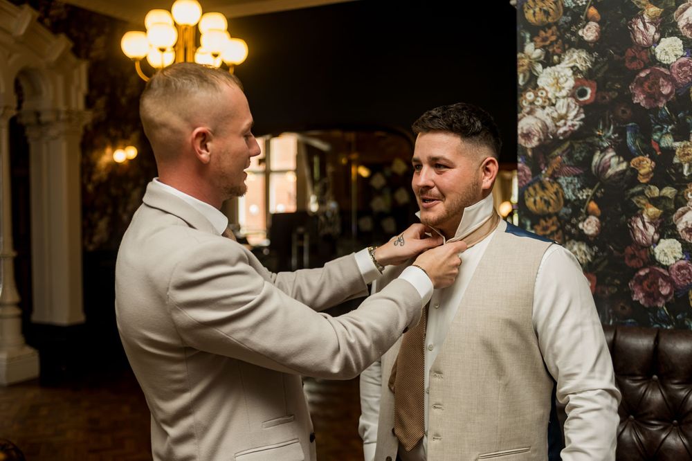 Groomsmen share laughs and celebrate in a venue with elegant chandelier lighting and floral wallpaper.