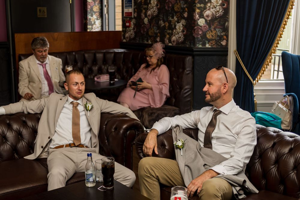 Wedding party members in light suits share drinks and conversation at a reception.