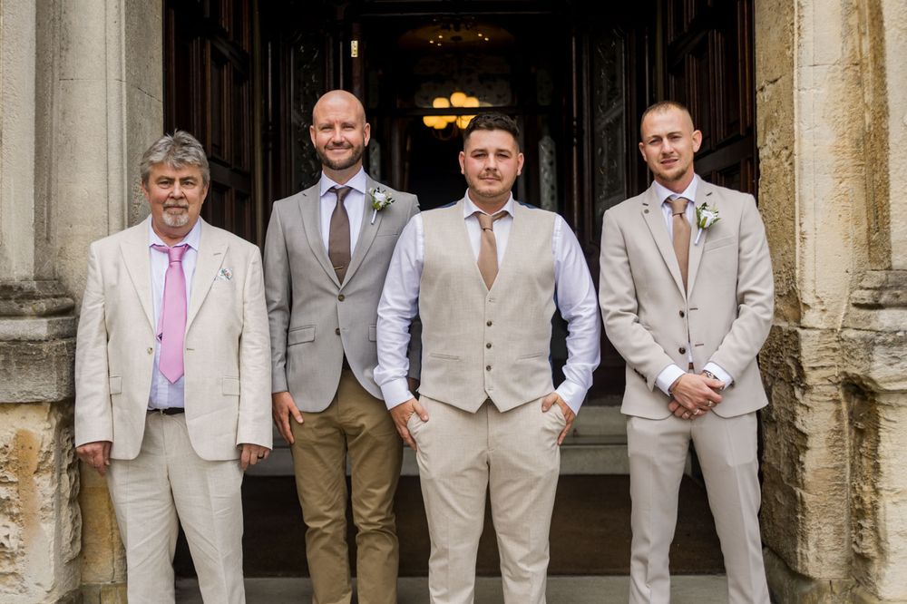 Wedding party members stand in formation under decorative stone archways.