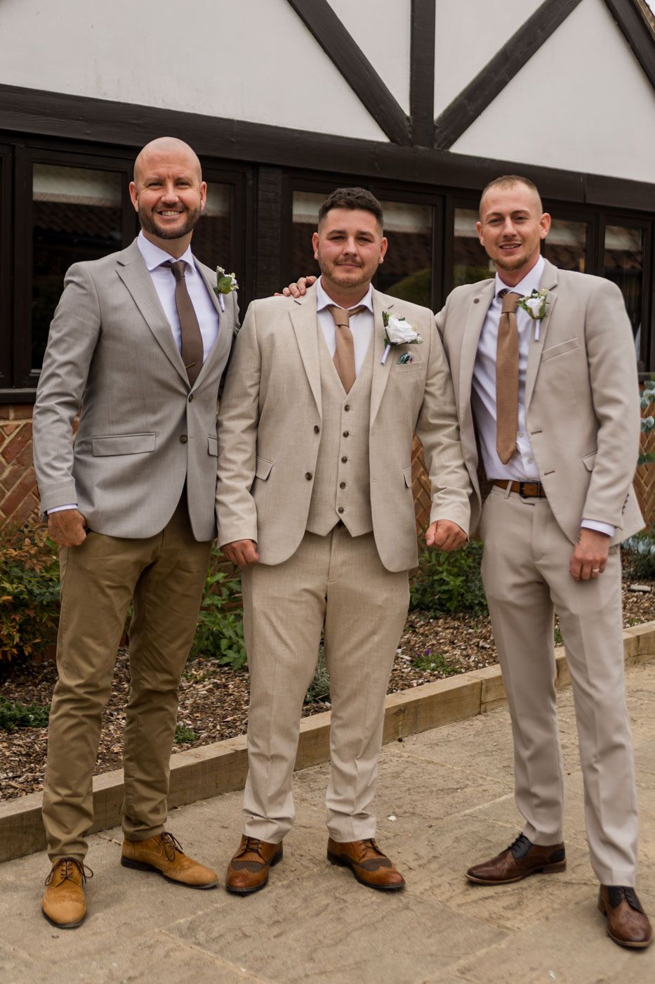 Groomsmen in coordinating beige and tan suits pose together on concrete path.