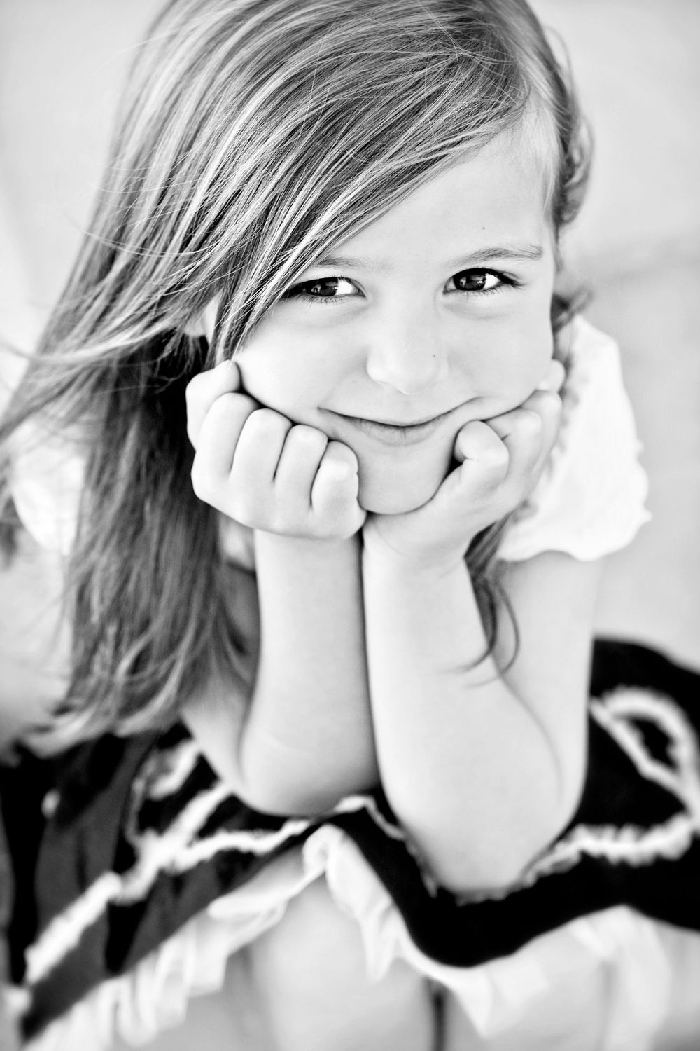 black and white photo of a young girl smiling at the camera with her hands on her cheeks