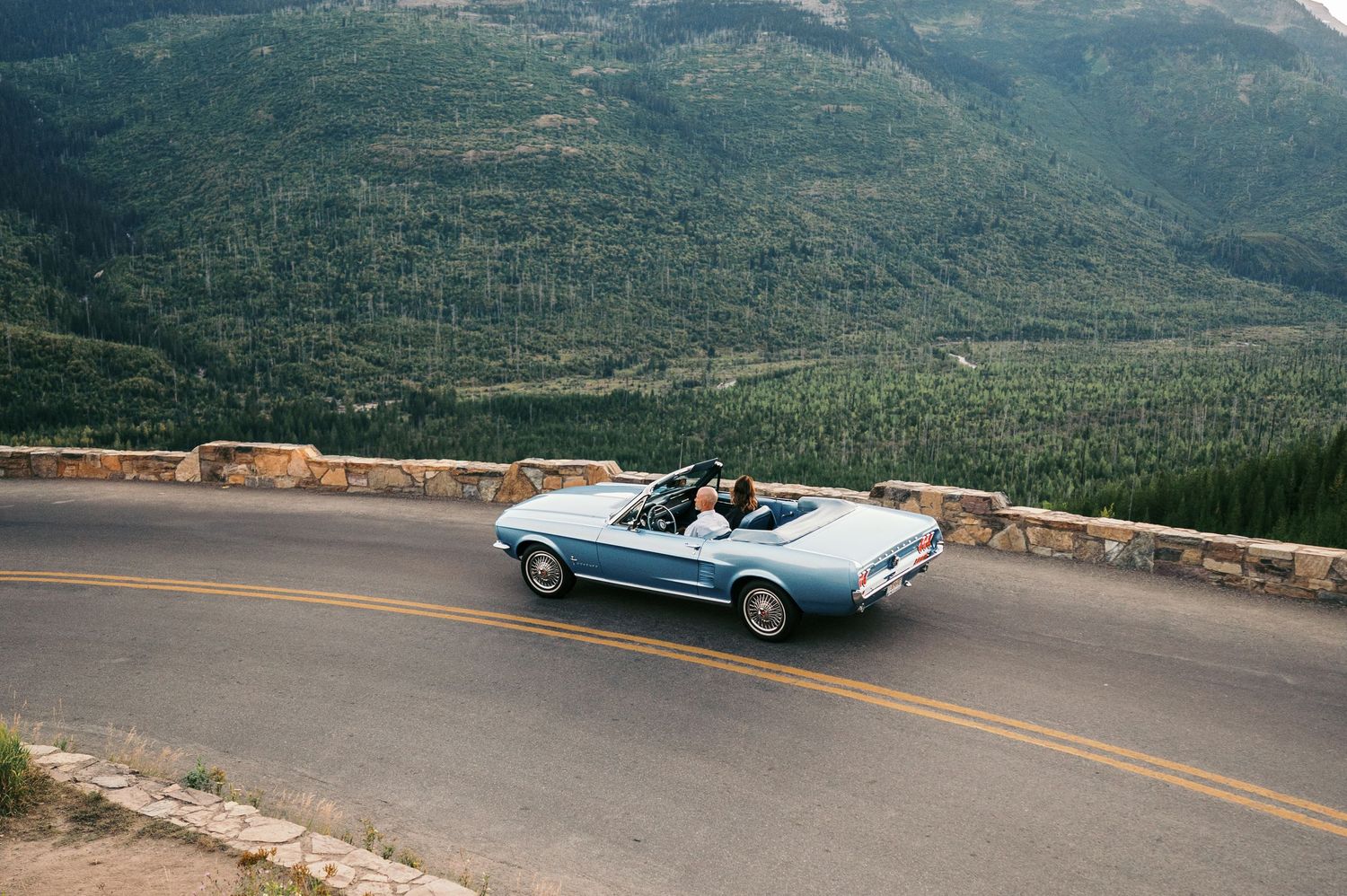 A panoramic sequence of a classic convertible car driving along a scenic mountain road with sweeping valley views.