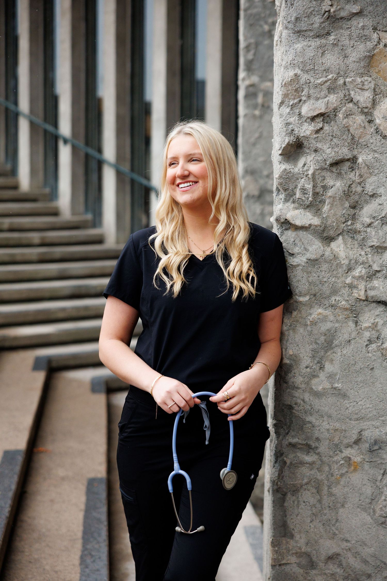 A series of professional portraits showing someone in black scrubs and a stethoscope sitting and smiling on stone steps.
