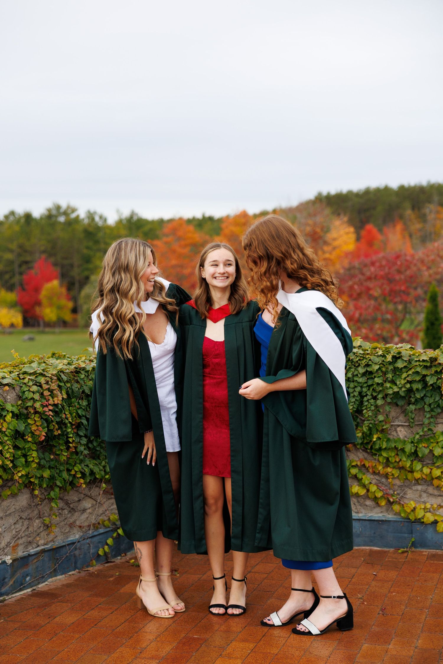 A group of friends laugh together while sitting on brick steps surrounded by autumn foliage and colorful trees.