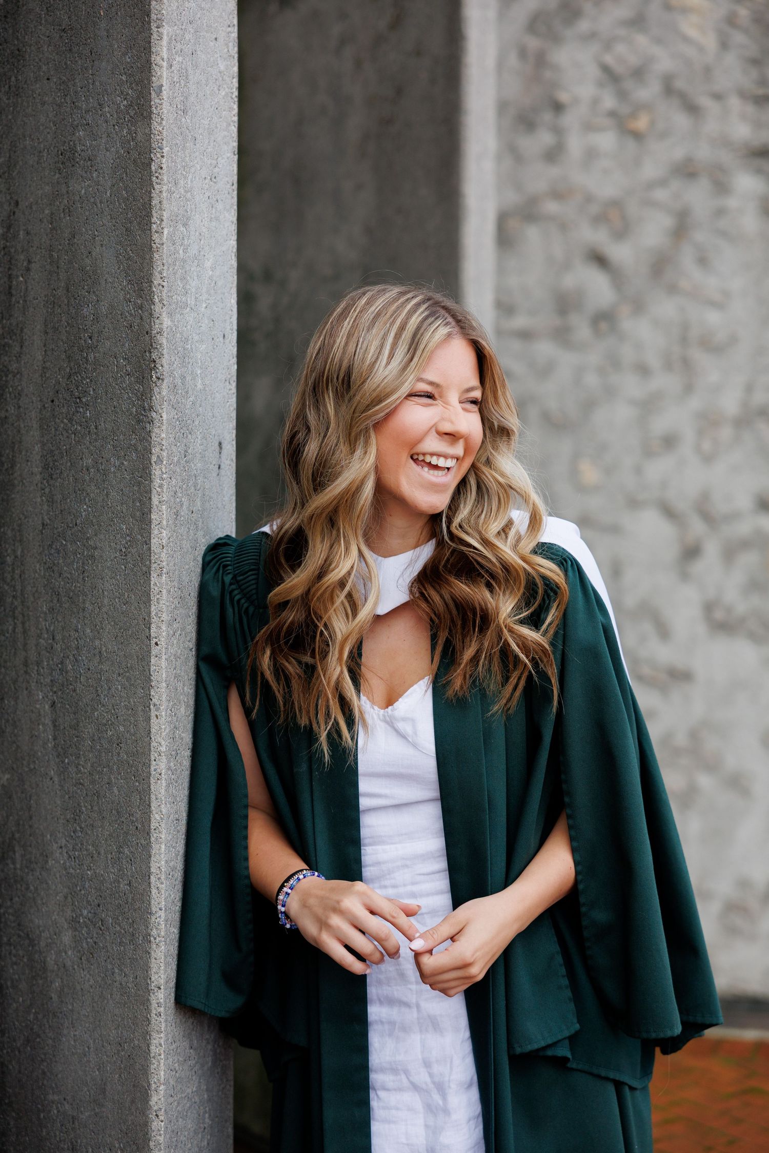 Professional headshot portrait against stone wall background wearing dark green blazer and white top.