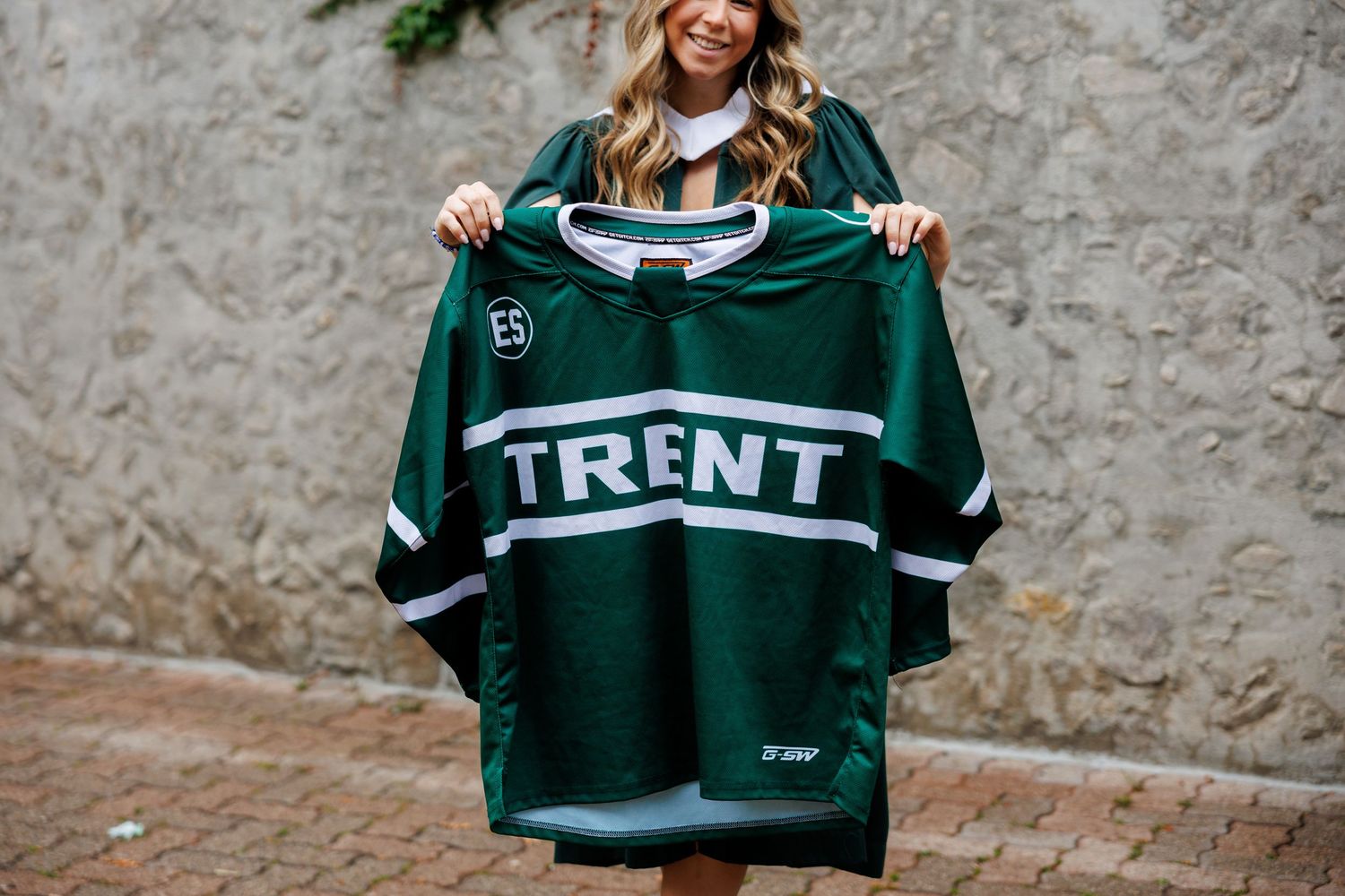 A person shows off a collection of green and white sports jerseys hanging against a gray wall.