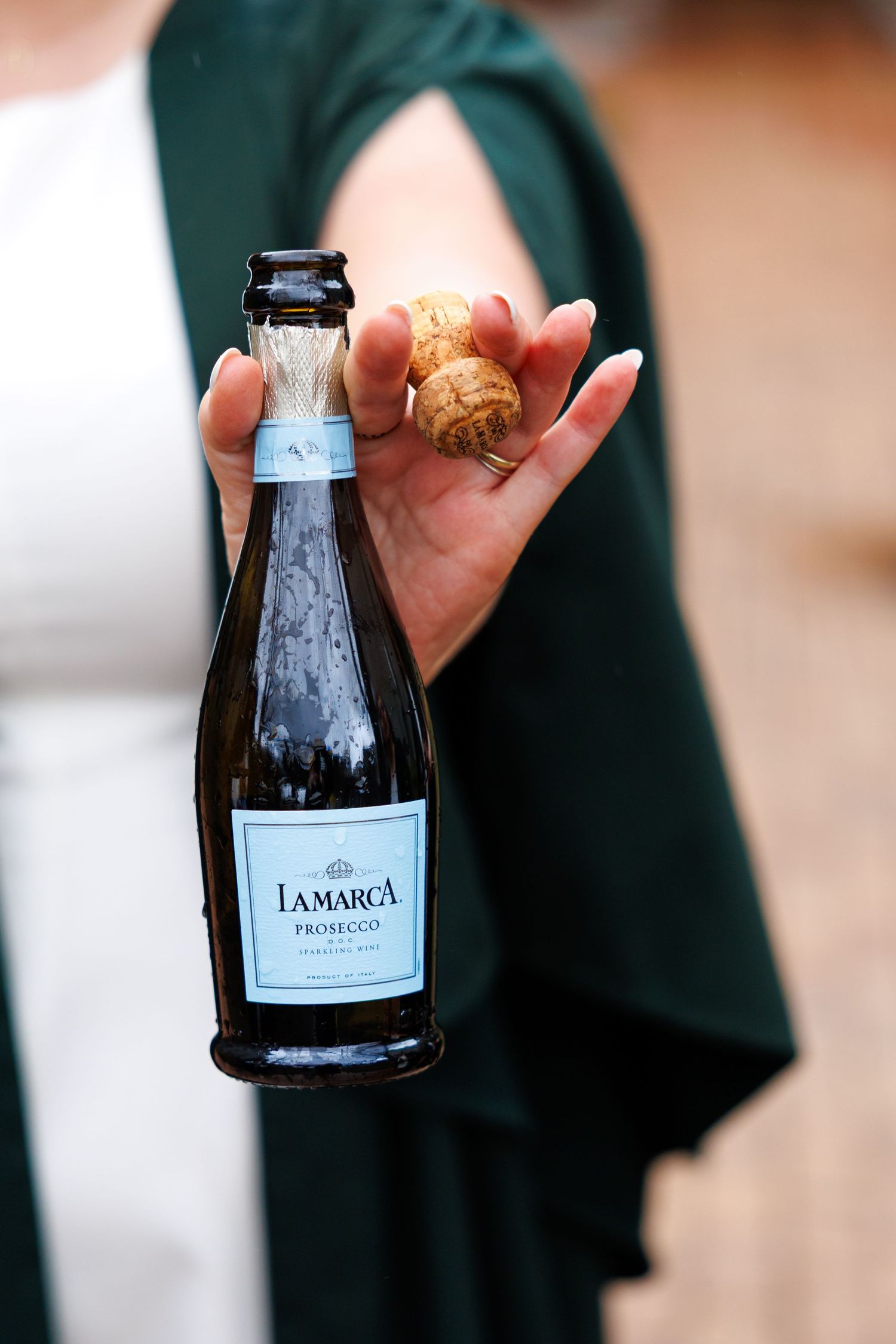 A hand holds a small bottle of Prosecco La Marca wine against a dark background.