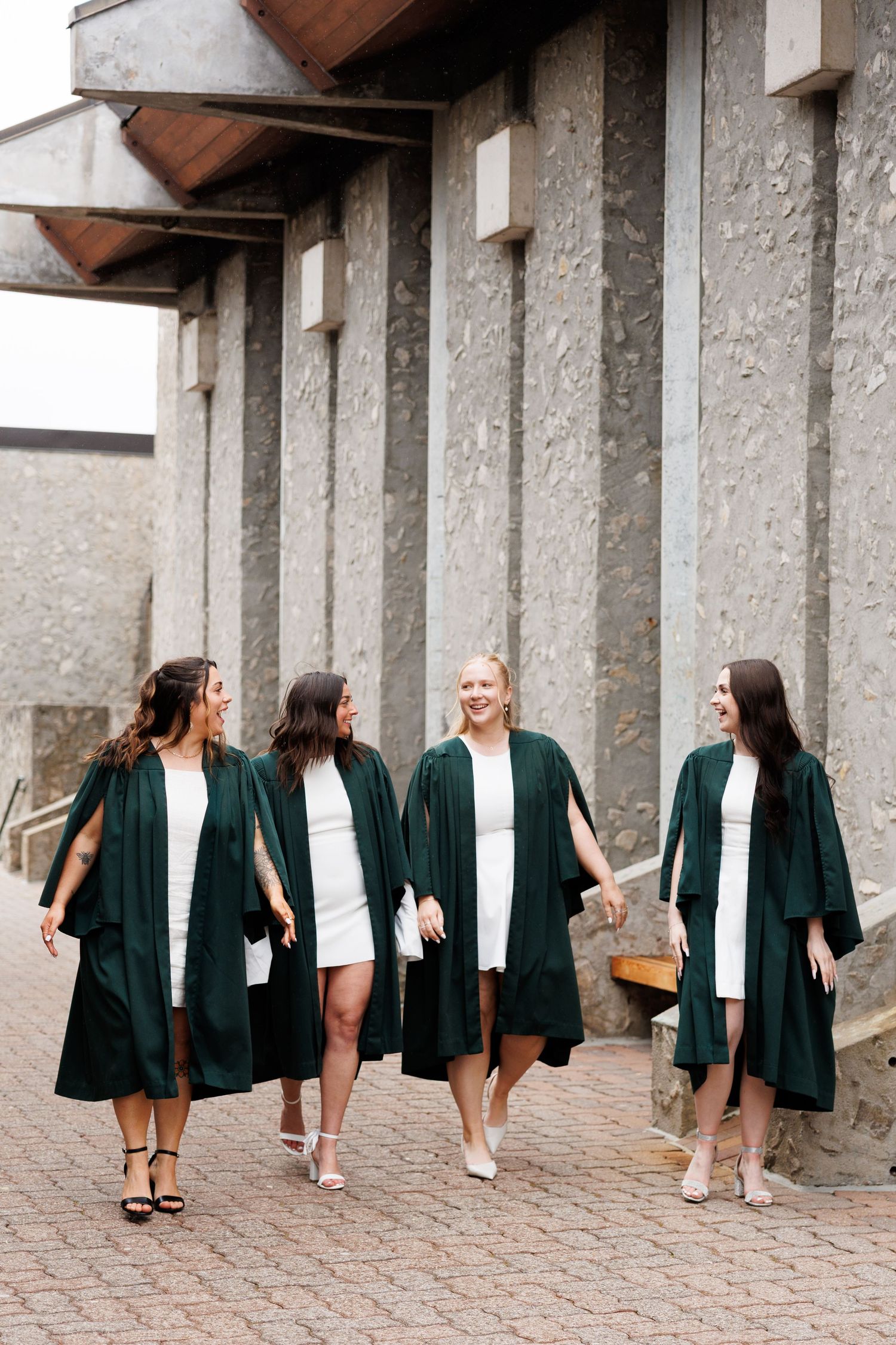 A creative sequence of photos showing five graduation gowns hung in a row along a stone wall.