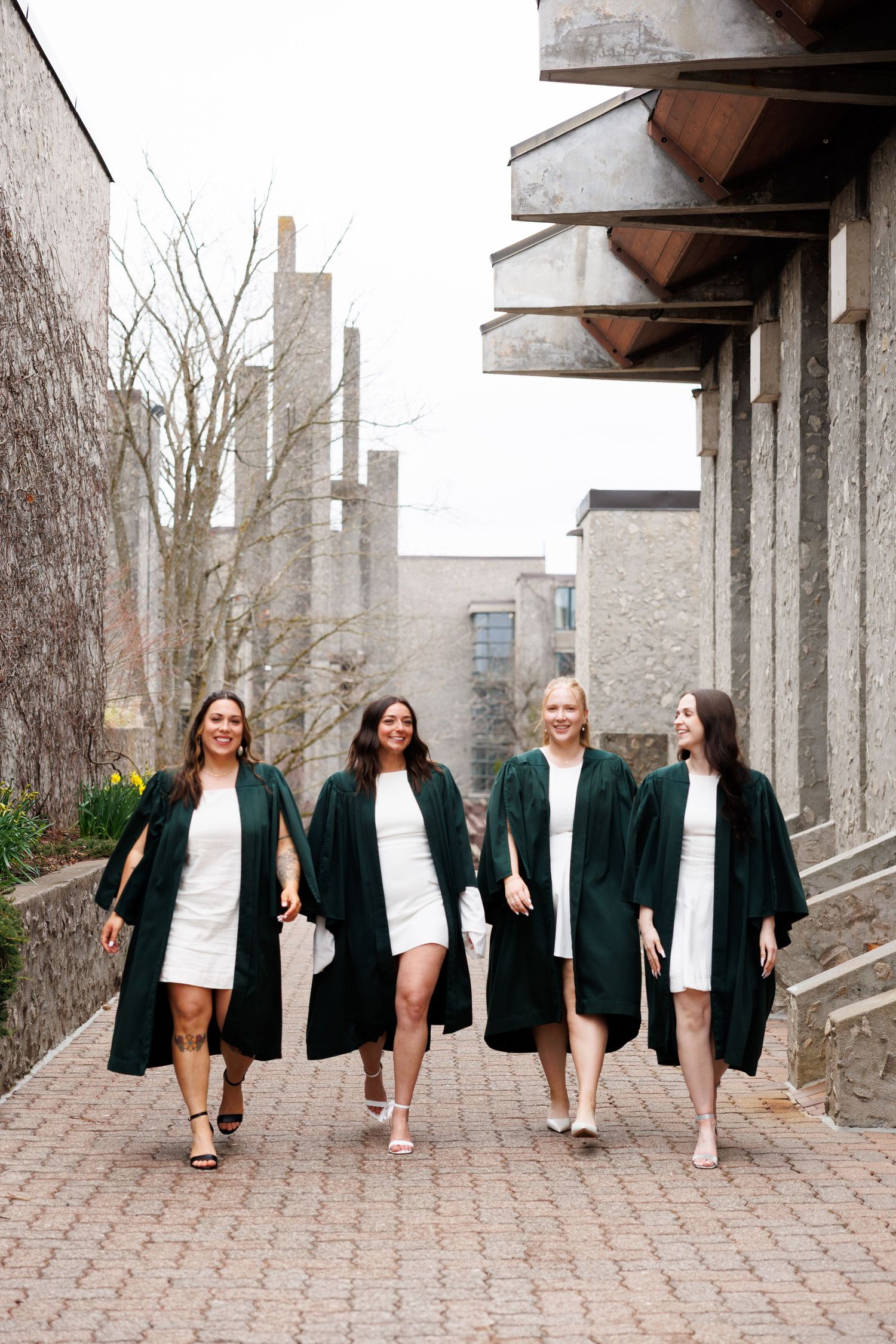 A group wearing matching dark blazers and light dresses pose together on a brick walkway for graduation photos.
