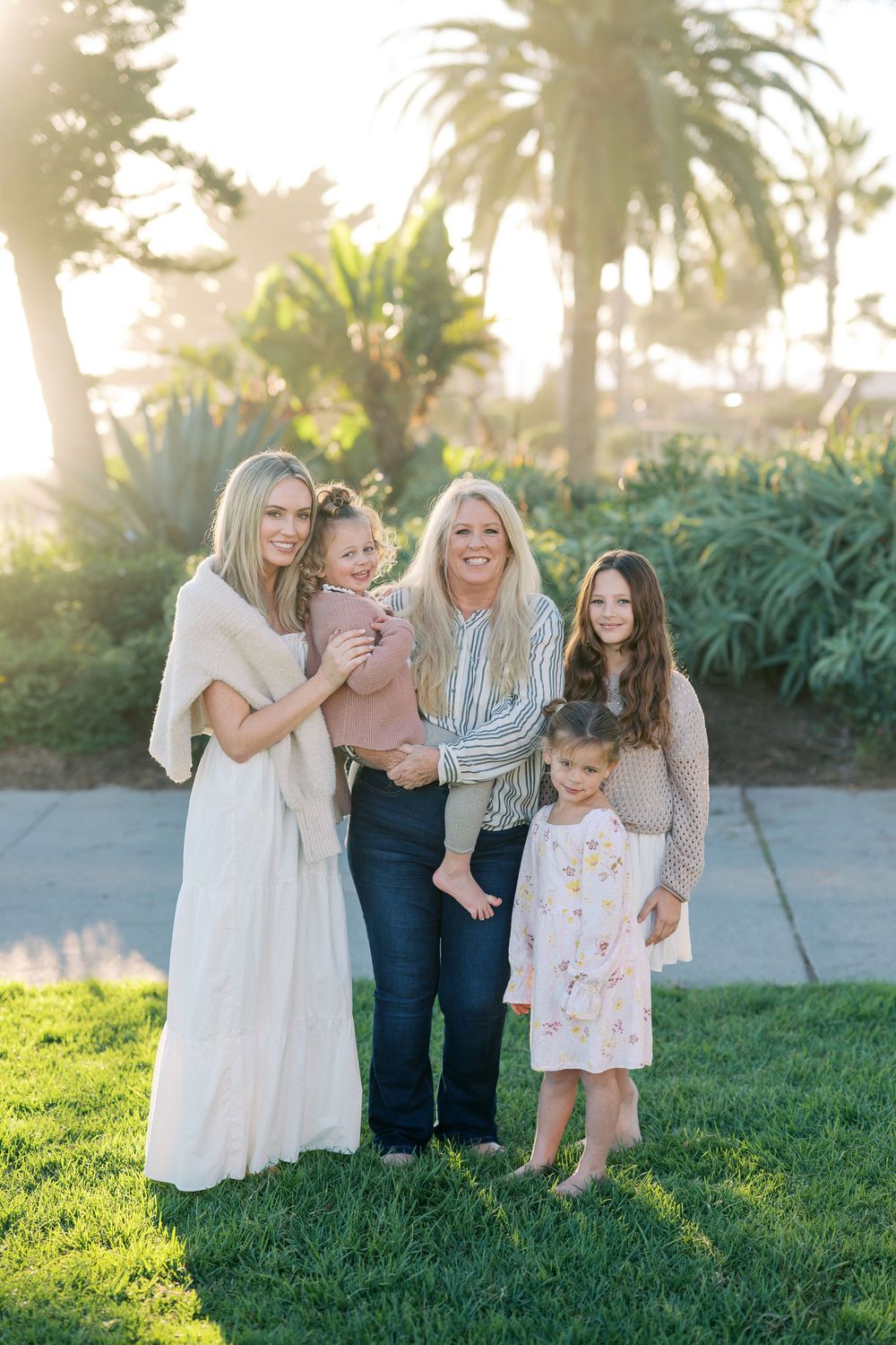 Family portrait outdoors in a garden setting with palm trees and lush greenery during golden hour lighting.