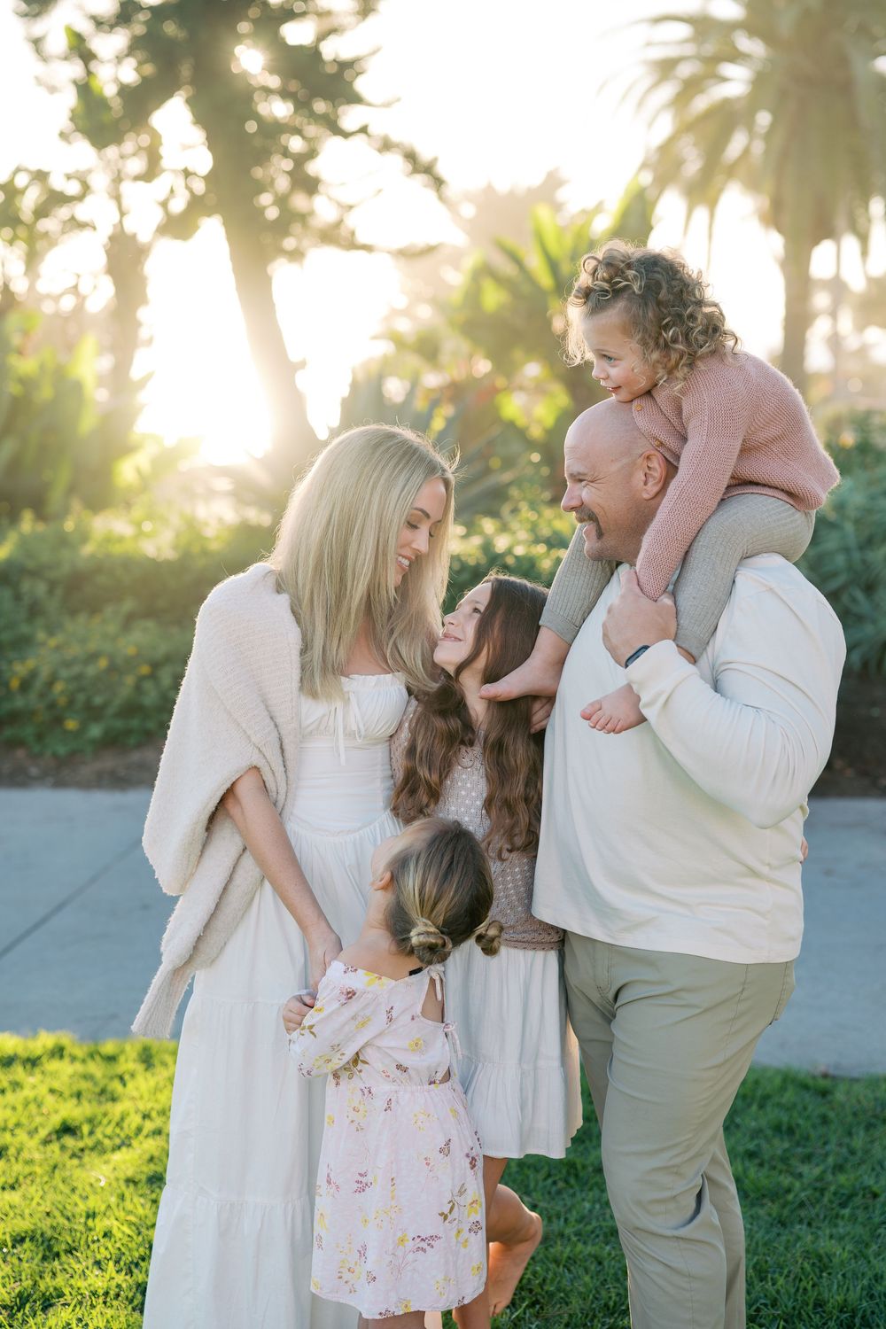 A family shares tender moments together outdoors at sunset in matching white and neutral outfits.
