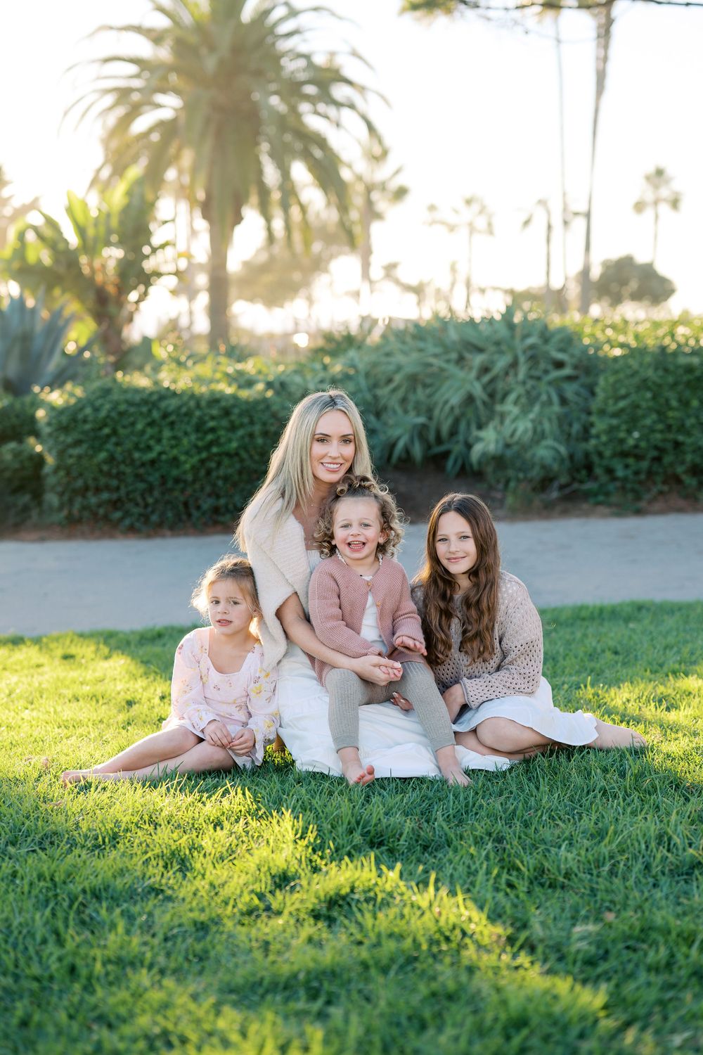 A family group sits together on lush grass with palm trees in the background during golden hour.