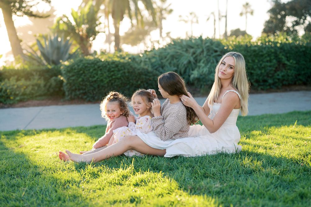 A group lies together on green grass during a sunny golden hour photoshoot in a park.