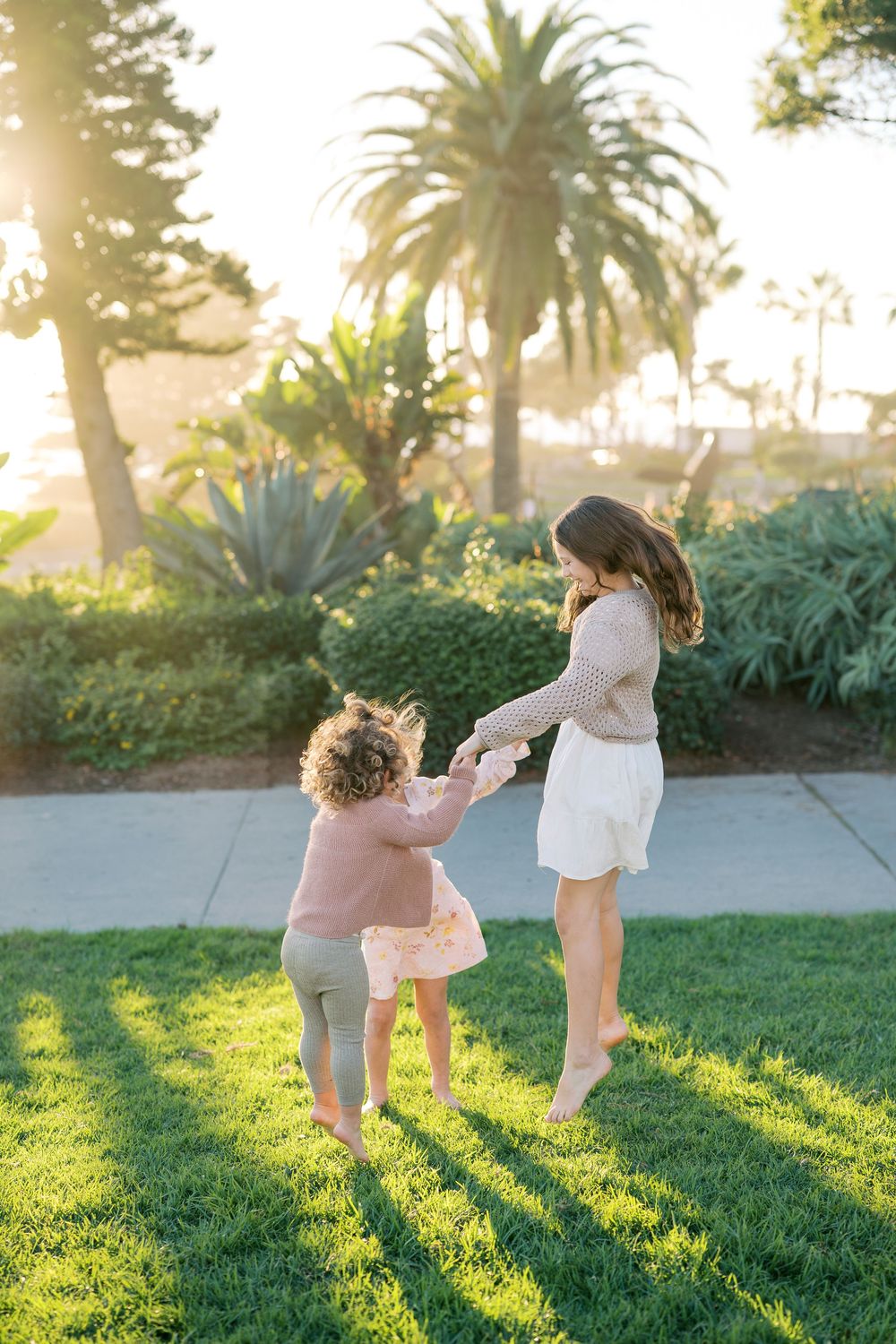 Two people play together on a grassy lawn at sunset with palm trees in the background.