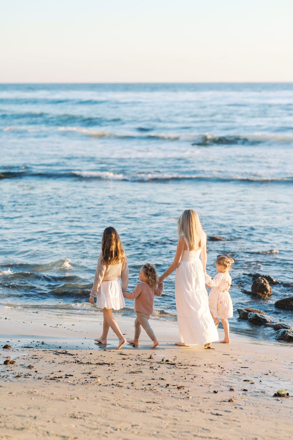 A serene beach scene at sunset with people walking along the shoreline near rocky outcrops.