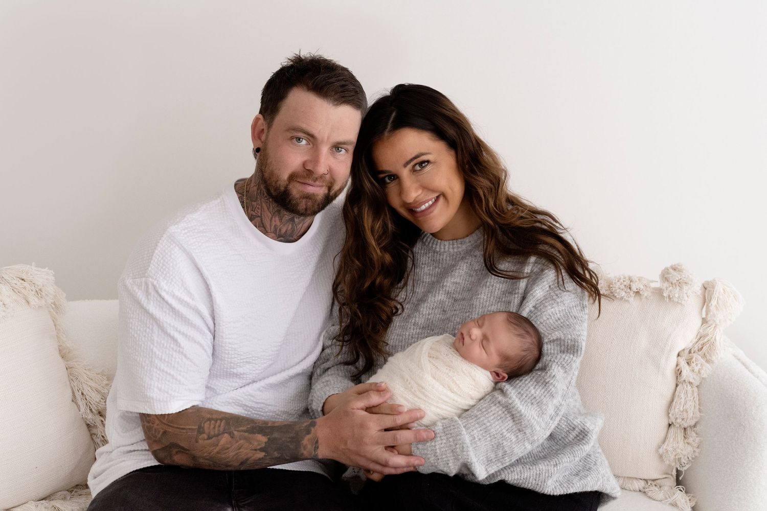 A family sitting together on a white couch in matching neutral outfits for an intimate lifestyle photoshoot.