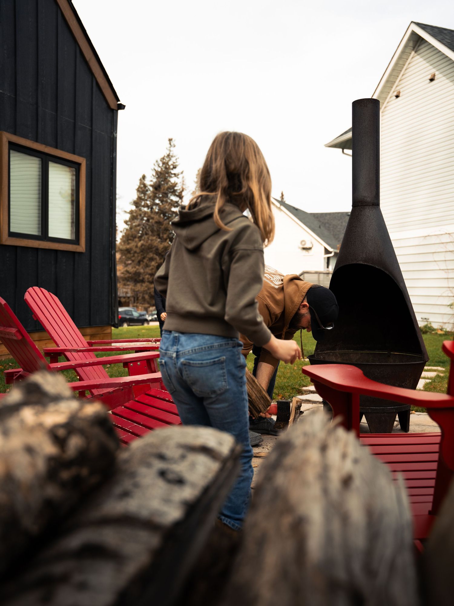 Red Adirondack chairs outside modern black cabin at dusk.